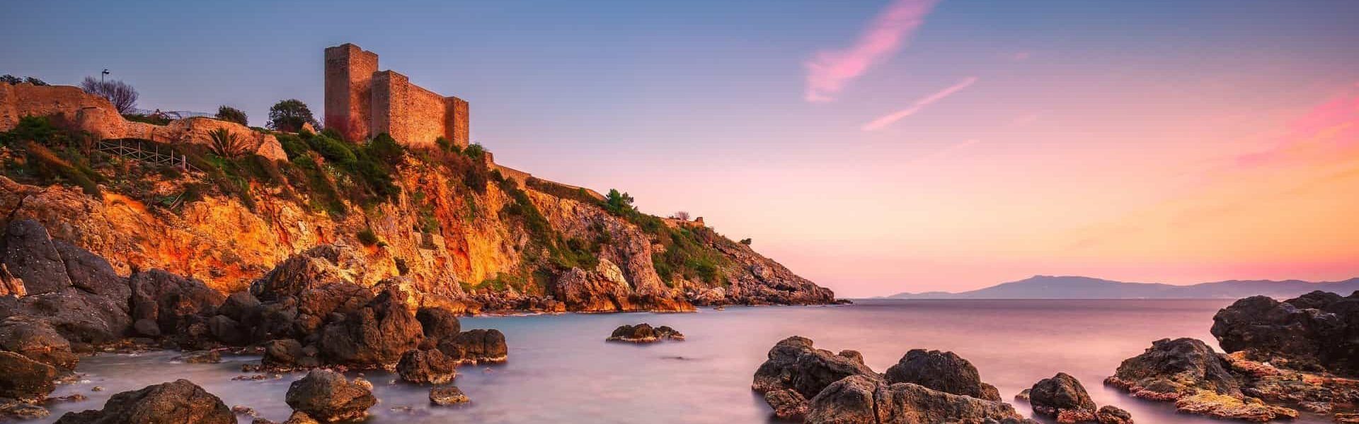 Talamone rock beach medieval fortress  sunset. Maremma Argentario, Tuscany, Italy